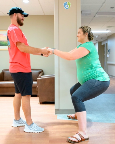 pregnant woman squatting while holding husbands hands